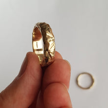 Load image into Gallery viewer, A chunky, textured wedding ring made from recycled 9ct yellow gold held in a hand.