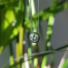 Load image into Gallery viewer, A diamond solitaire pendant with a silver chain attached, set on a blurred organic background.
